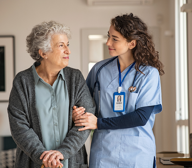 Young caregiver helping senior woman walking. Nurse assisting her old woman patient at nursing home. Senior woman with walking stick being helped by nurse at home.